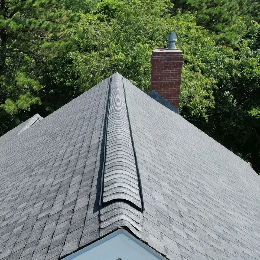 Newly installed asphalt shingle roof with ridge vent and a brick chimney.
