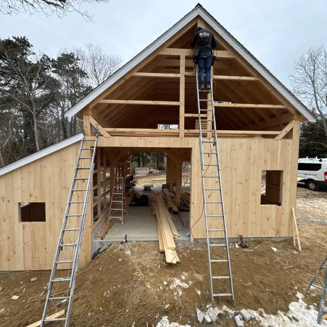 A wooden barn under construction with exposed beams and ladders.