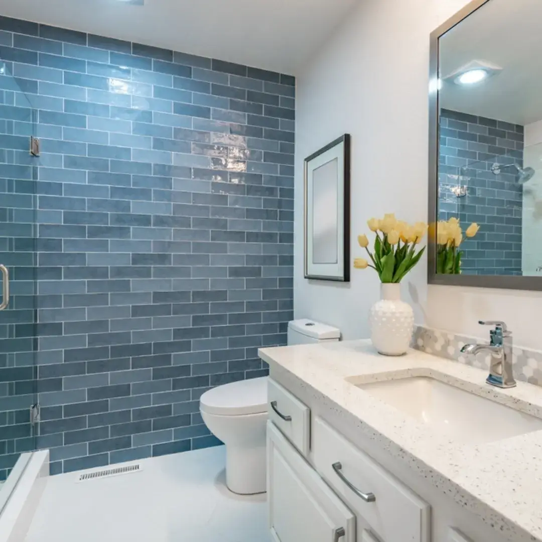 A stylish bathroom with a blue subway tile accent wall, white vanity and glass shower.