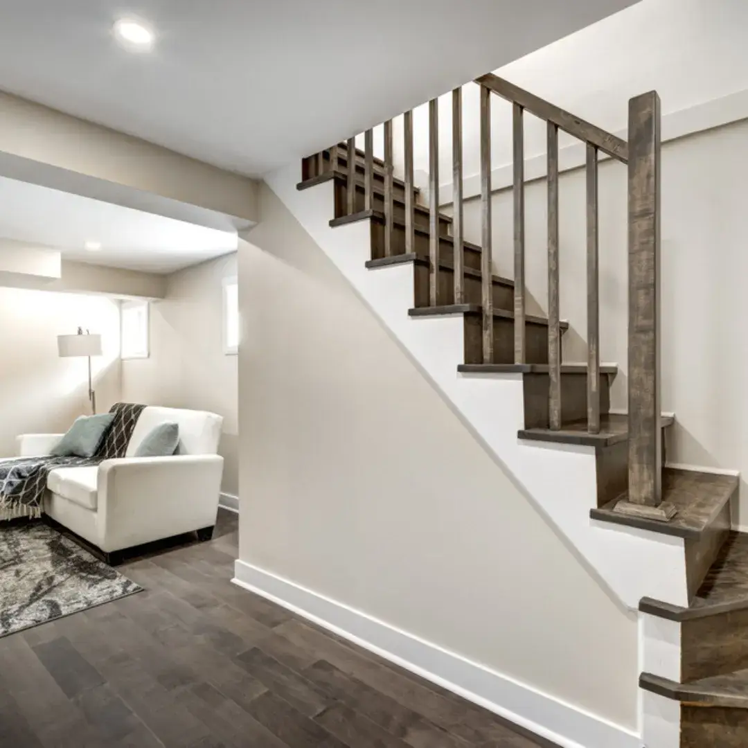 Basement with wooden staircase, white armchair and a cozy reading nook.