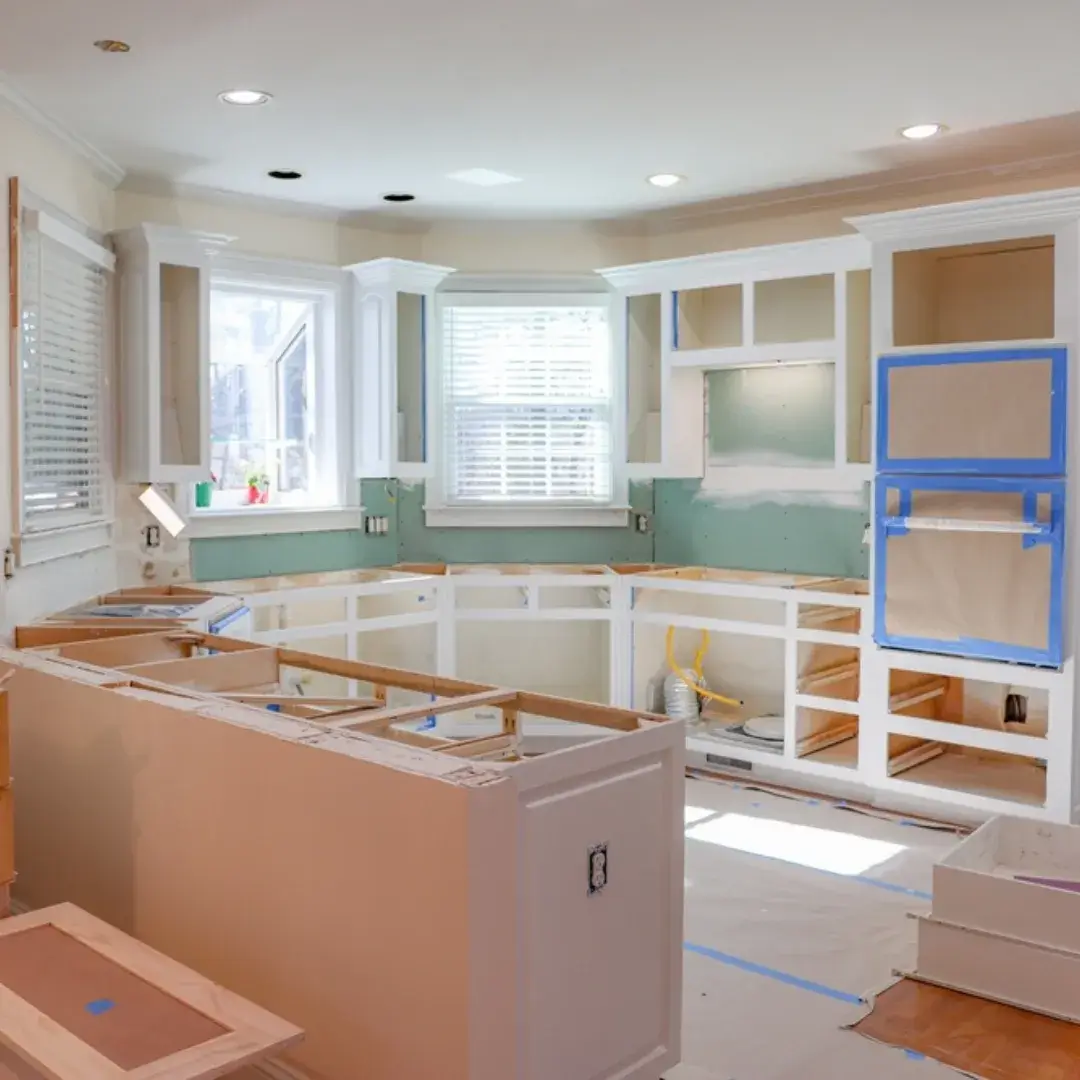 A kitchen undergoing renovation with white cabinets being installed and walls prepped for painting.