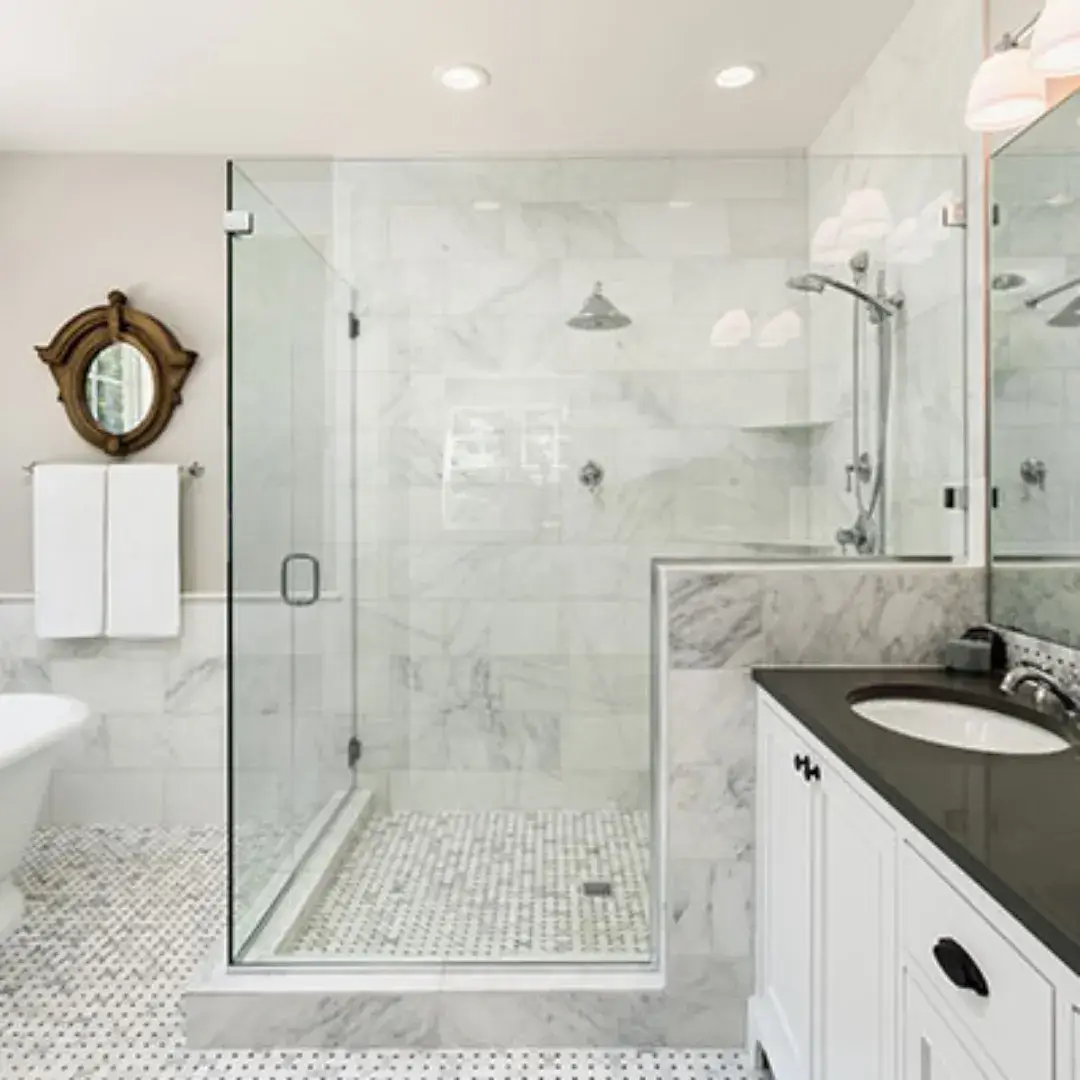Elegant bathroom with a glass-enclosed shower, marble tiles and a sleek vanity with a black countertop.