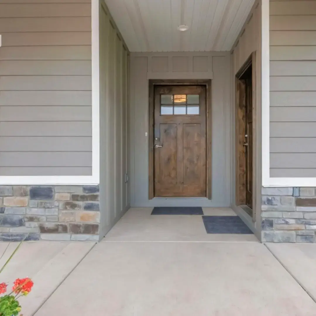 A modern home entryway featuring a rustic wooden front door, gray siding and stone accents.