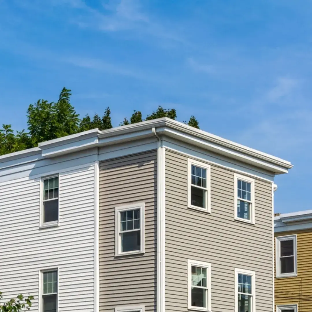 A multi-story residential building with beige and white vinyl siding, featuring multiple windows.