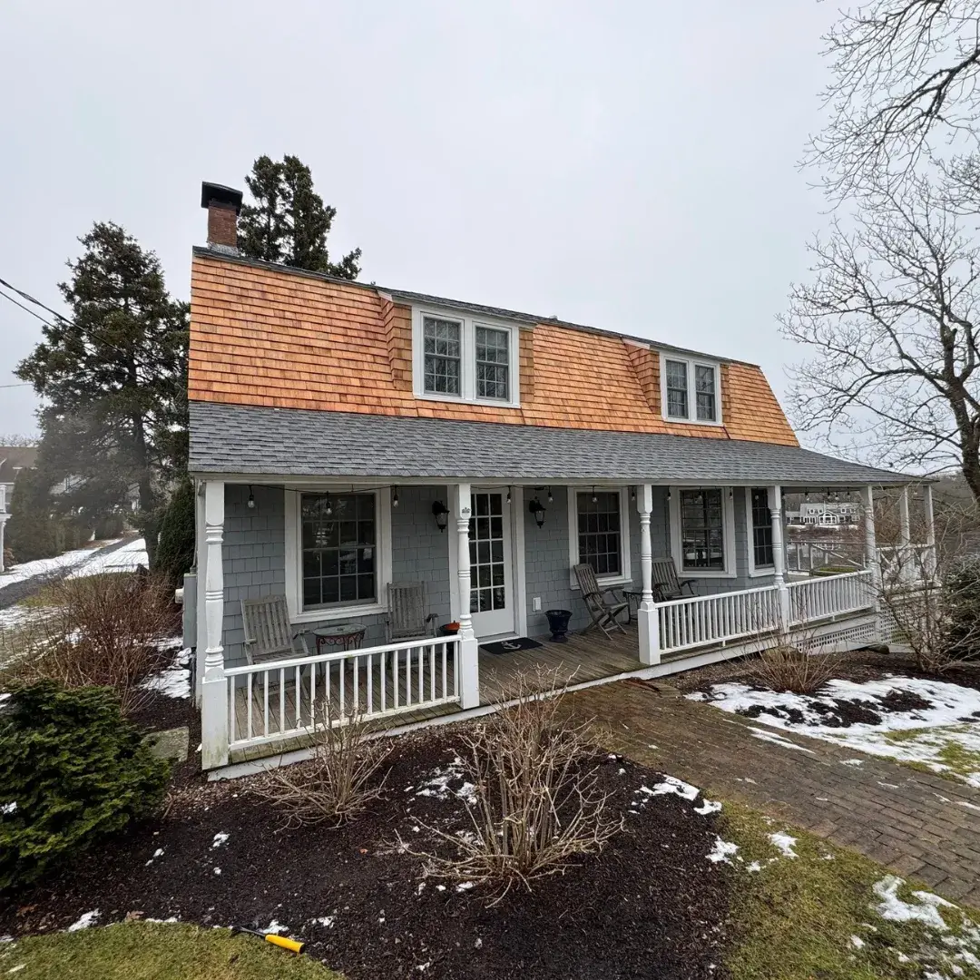 A traditional-style house with a covered porch, gray siding and a newly installed cedar shingle roof.