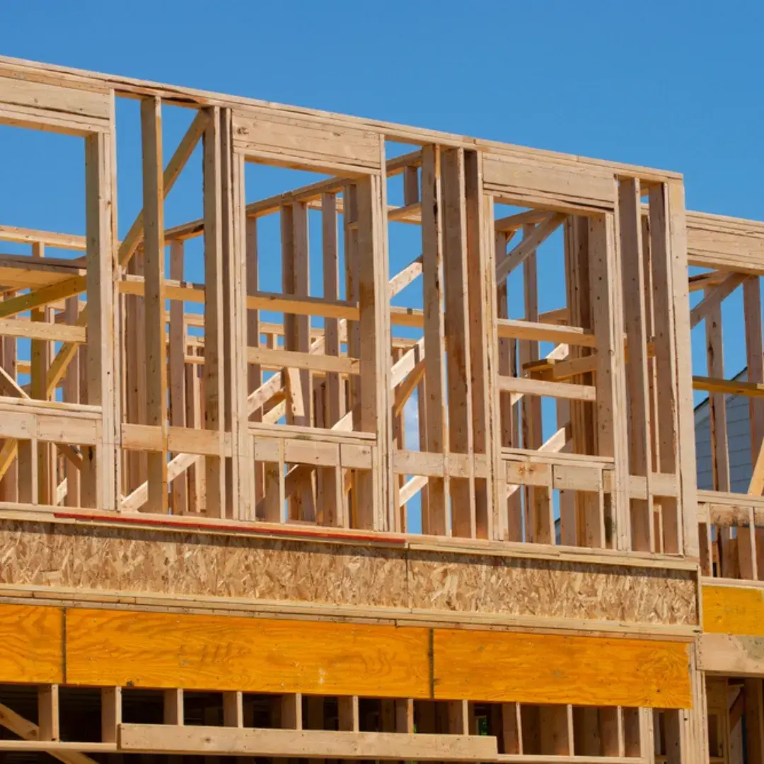 Wooden framing of a house under construction with a clear blue sky in the background.