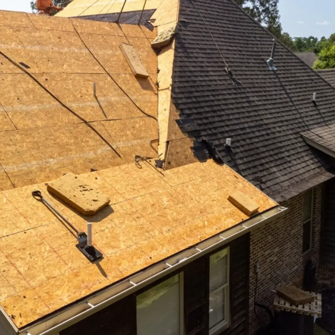 A home undergoing a roof replacement with exposed wooden sheathing and new asphalt shingles being installed.