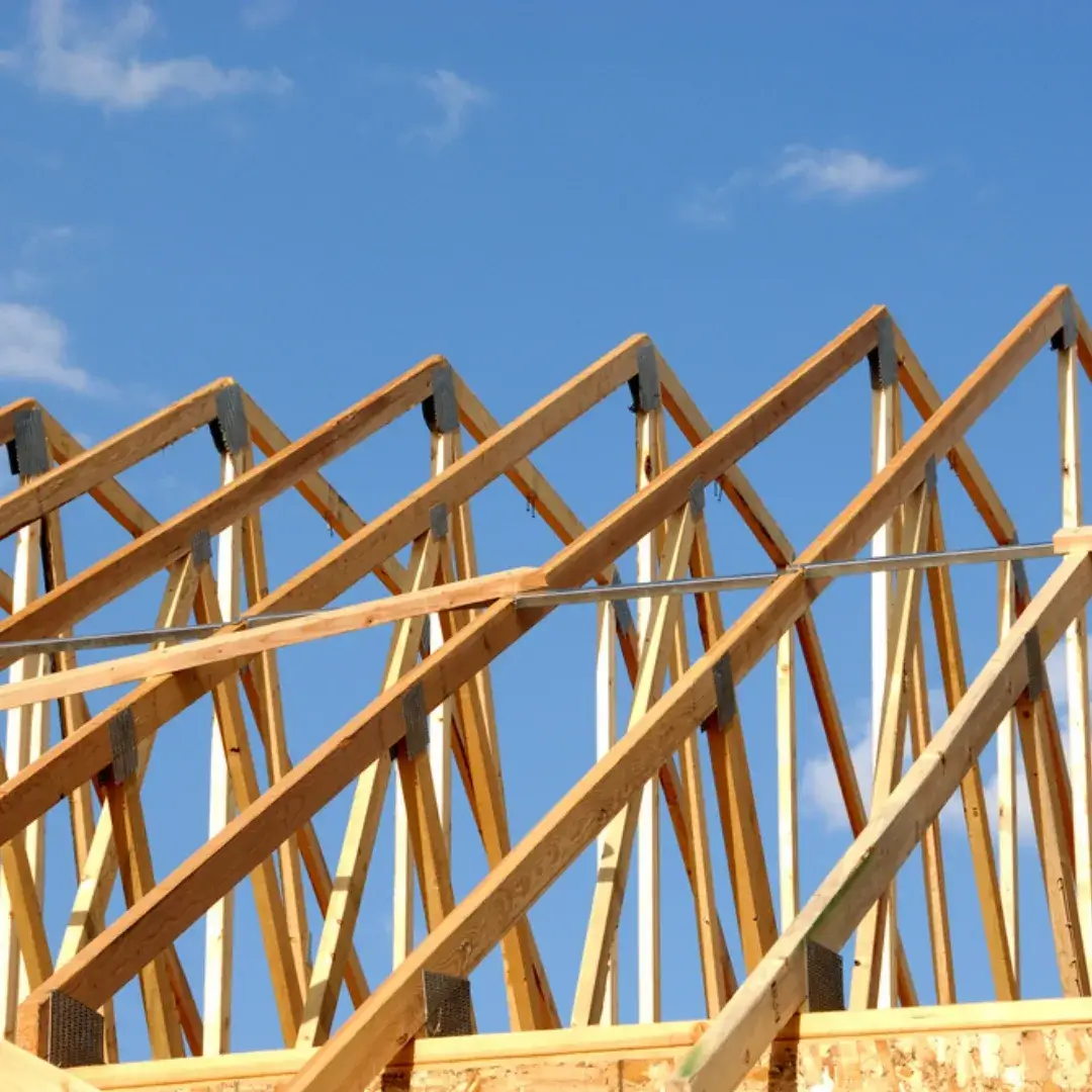 Angled wooden roof trusses installed on a house under construction with a blue sky in the background.