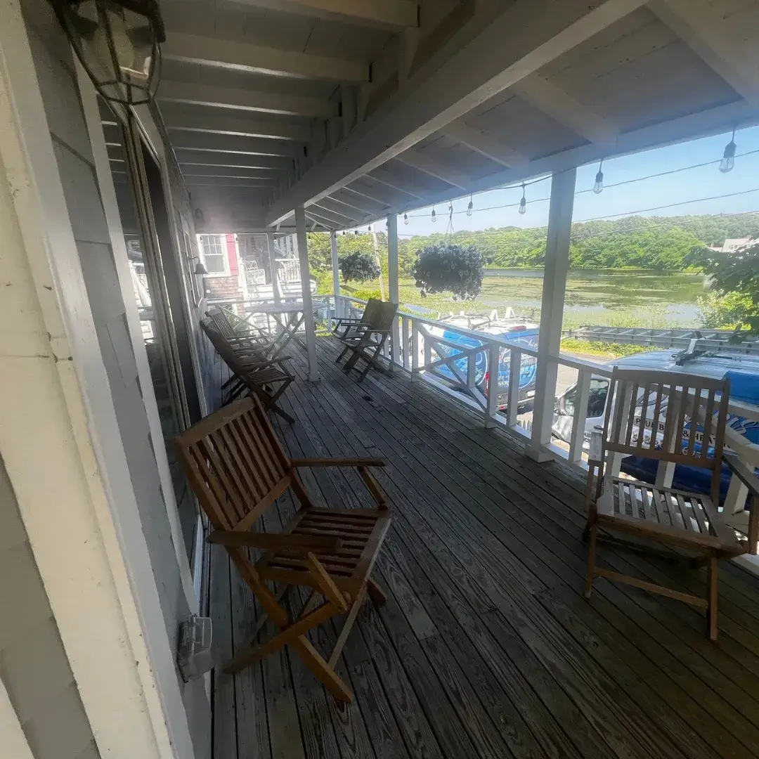 A scenic covered porch with wooden chairs overlooking a waterfront area.