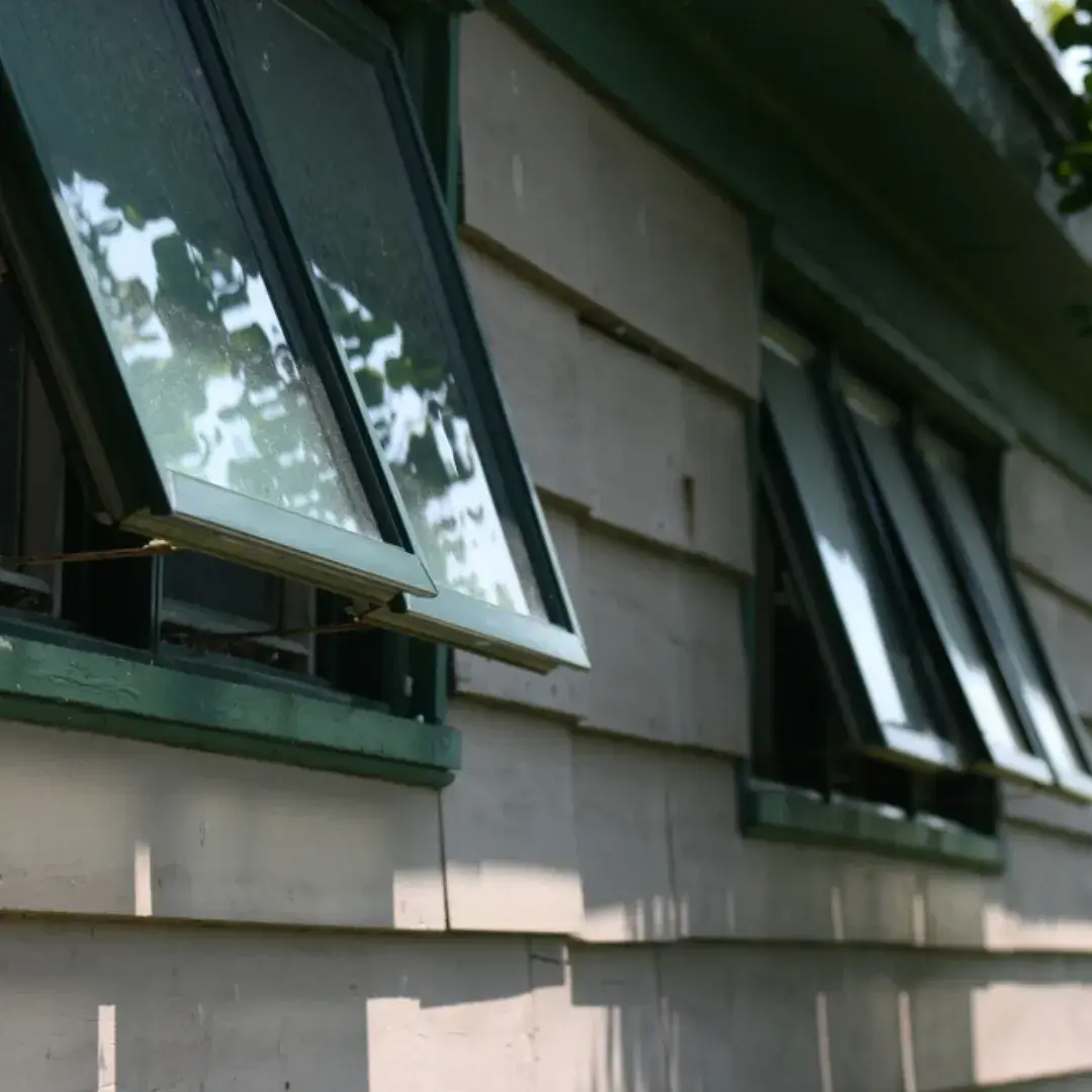 Green awning windows on an old wooden house exterior, slightly open for ventilation.