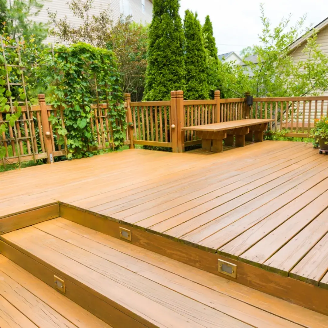 A spacious wooden deck with built-in seating, surrounded by lush greenery and a wooden fence.