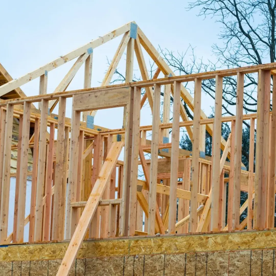 A partially built house with wooden roof trusses and wall framing under a cloudy sky.